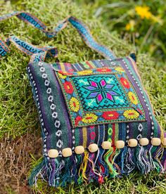 a colorful bag with tassels is laying on the ground next to some grass