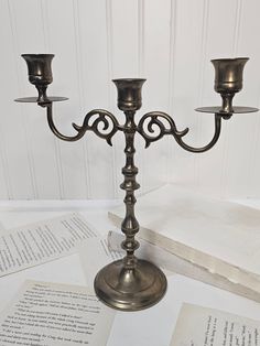 a metal candelabra sitting on top of an open book next to two candles