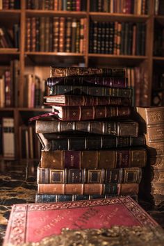 a stack of books sitting on top of a table in front of a book shelf