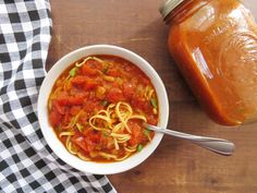 a white bowl filled with pasta and sauce next to a jar of tomato sauce on a wooden table