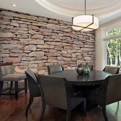 a dining room table with chairs and a vase on it in front of a stone wall