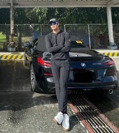 a man standing next to a bmw car in front of a parking garage with his arms crossed