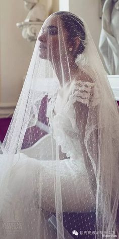 a woman in a wedding dress and veil sitting on a chair with her hands under the veil