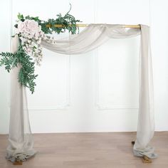 two tall vases with flowers and greenery on them are sitting in front of a white wall