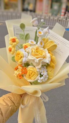 a bouquet of yellow and white flowers is held by someone's hand on the street