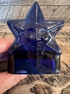 a hand holding a blue glass object with a star on it's face in front of a wooden background