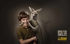 a young boy poses with a kangaroo in front of a wallpapered background that says open for smiles