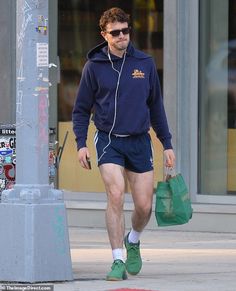 a man walking down the street with headphones on, carrying shopping bags and wearing shorts