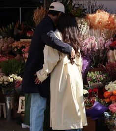 a man and woman are kissing in front of a flower stand with lots of flowers