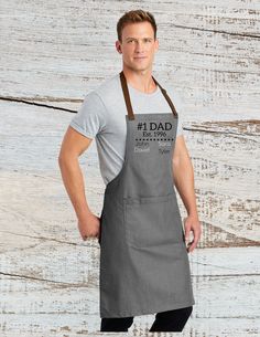 a man standing in front of a wooden wall wearing an apron with the words dad on it