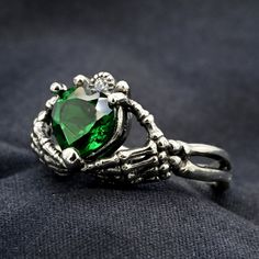 a ring with a heart shaped green stone in the center on a black cloth background