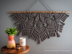 a wooden table with a vase and plant on it next to a decorative wall hanging