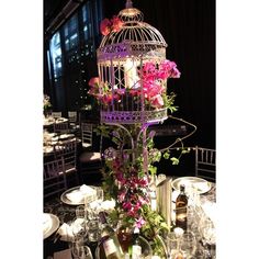 a birdcage filled with pink flowers and wine bottles on top of a table