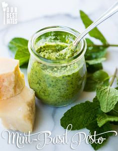 mint basil pesto in a glass jar next to two pieces of cheese and green leaves