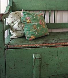 an old green bench with two pillows on it's back and one pillow on the seat