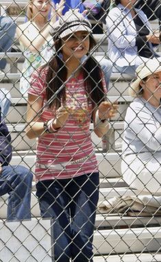 a girl is standing behind a fence with her hand up to the camera and smiling