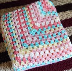 a crocheted dishcloth is laying on top of a striped blanket, which has multicolored squares