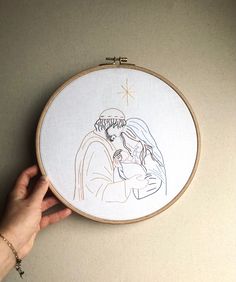 a hand is holding a embroidery hoop with a drawing of a man and woman