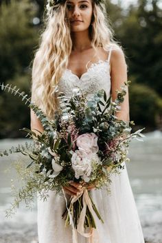 a woman in a wedding dress holding a bridal bouquet with greenery and flowers