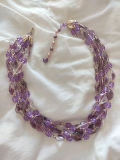 Necklace made up of 4 strands, each strand includes resin elements, in the shape of a small rhombus, in the following colours: purple, purple/transparent and transparent. They are interspersed with other smaller purple resin elements. The threads are gathered in a large, highly worked golden cap. It has an adjustable hook. The brand is written on the hook. The choker is signed HONG KONG. This choker is not the classic multi-strand choker: the difference in the color of the various elements, give Purple Multi-strand Beaded Necklace, Purple Multi-strand Necklace For Party, Adjustable Multi-strand Purple Beaded Necklaces, Elegant Multi-strand Purple Beaded Necklaces, Elegant Purple Multi-strand Beaded Necklaces, Purple Beads Necklace, Purple Bead Necklace, Purple Resin, Purple Beads