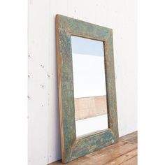 an old mirror sitting on top of a wooden table next to a white wall and wood floor