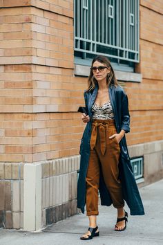 a woman is walking down the street wearing brown pants and a blue coat with black heels