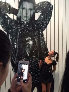 a woman taking a photo of herself in front of a wall with an advertisement on it