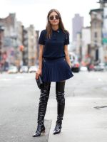 a woman in black boots and a blue shirt is standing on the street with her purse