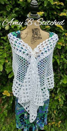 a white crocheted top with blue and green shorts on display in front of some bushes