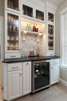 a kitchen with white cabinets and black counter tops, wine glasses on the glass shelves