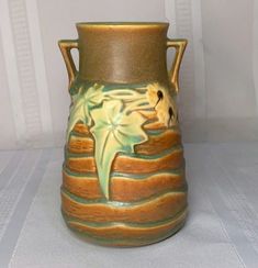 a brown and green vase sitting on top of a white table next to a wall