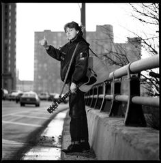 a man standing on the side of a road holding an electric guitar