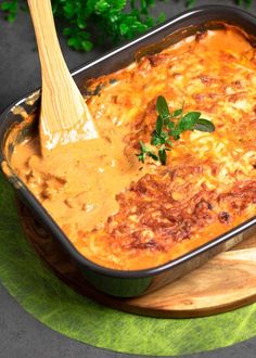 a casserole dish with meat and cheese in a wooden spatula on a green place mat