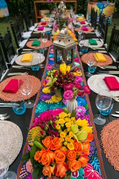 a long table is decorated with colorful flowers and place settings for an outdoor dinner party