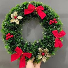 a hand holding a christmas wreath with red bows