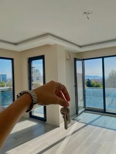 a hand holding a key in front of an open room with large windows and sliding glass doors