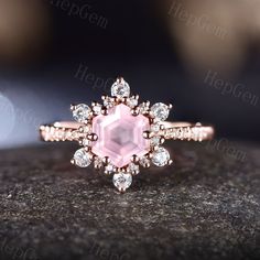 a pink diamond ring sitting on top of a black stone surface with diamonds around it