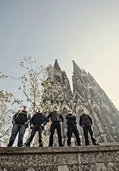 a group of men standing on top of a stone wall next to a tall building