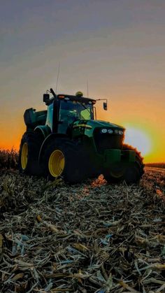 a tractor is parked in the middle of a corn field as the sun goes down