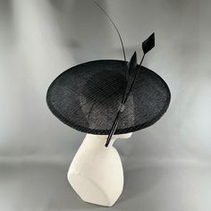 A seductive Dior style saucer in black sinamay strawcloth, with silver lurex thread. Simply and strikingly trimmed with two arrow feathers and one ostrich quill in black. Elastic and comb attachment for easy, comfortable wear. Lifted Millinery headwear is constructed with time honored techniques and fine craftsmanship. All hats are meticulously blocked and sewn by hand without the use of adhesives to attach trims. This ensures a long lasting hat with the ability to be retrimmed throughout the ye Black Mini Hat With Feather Trim For Royal Ascot, Evening Fascinator With Feather Trim, Black Fascinator With Curved Brim For Formal Occasions, Black Sinamay Fascinator For Kentucky Derby, Black Curved Brim Fascinator For Formal Occasions, Black Feathered Hats For Royal Ascot, Black Formal Fascinator With Curved Brim, Black Hats With Feathers For Royal Ascot, Elegant Evening Fascinator With Feather Trim