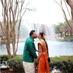 a man and woman standing next to each other in front of a lake with trees