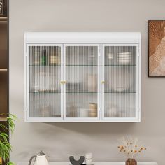 a white cabinet with glass doors on the wall in a kitchen next to a potted plant