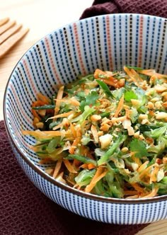 a blue and white bowl filled with salad on top of a wooden table next to utensils