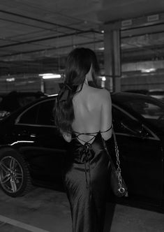 a woman in a black dress is walking towards a car with her back to the camera