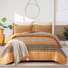 a bed with an orange and yellow comforter in a room next to potted plants