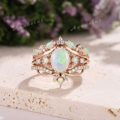 an opal and diamond ring sits on top of a stone slab with flowers in the background