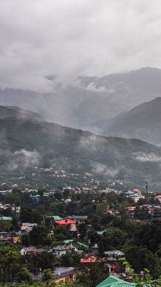 a city with mountains in the background and houses on the hillsides below, surrounded by clouds