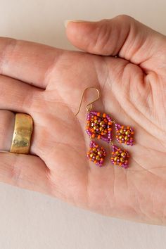 a woman's hand holding three small beaded earrings in gold, pink and orange