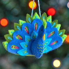 a blue and green bird ornament hanging from a christmas tree with lights in the background