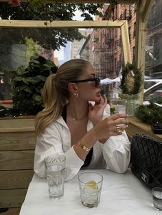 a woman sitting at a table in front of a window holding a cell phone to her ear